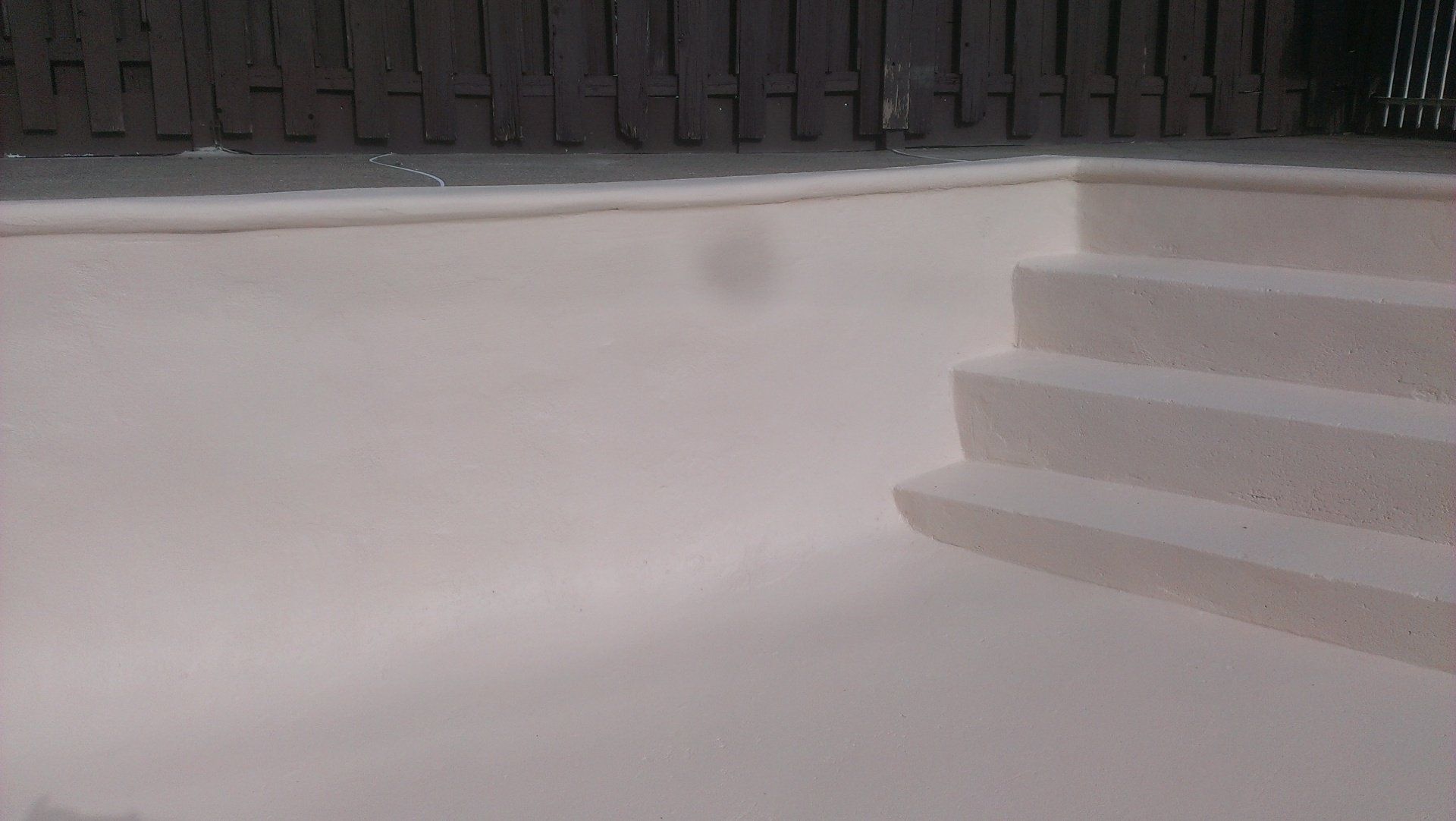 Une piscine blanche avec des escaliers et une clôture en bois en arrière-plan.