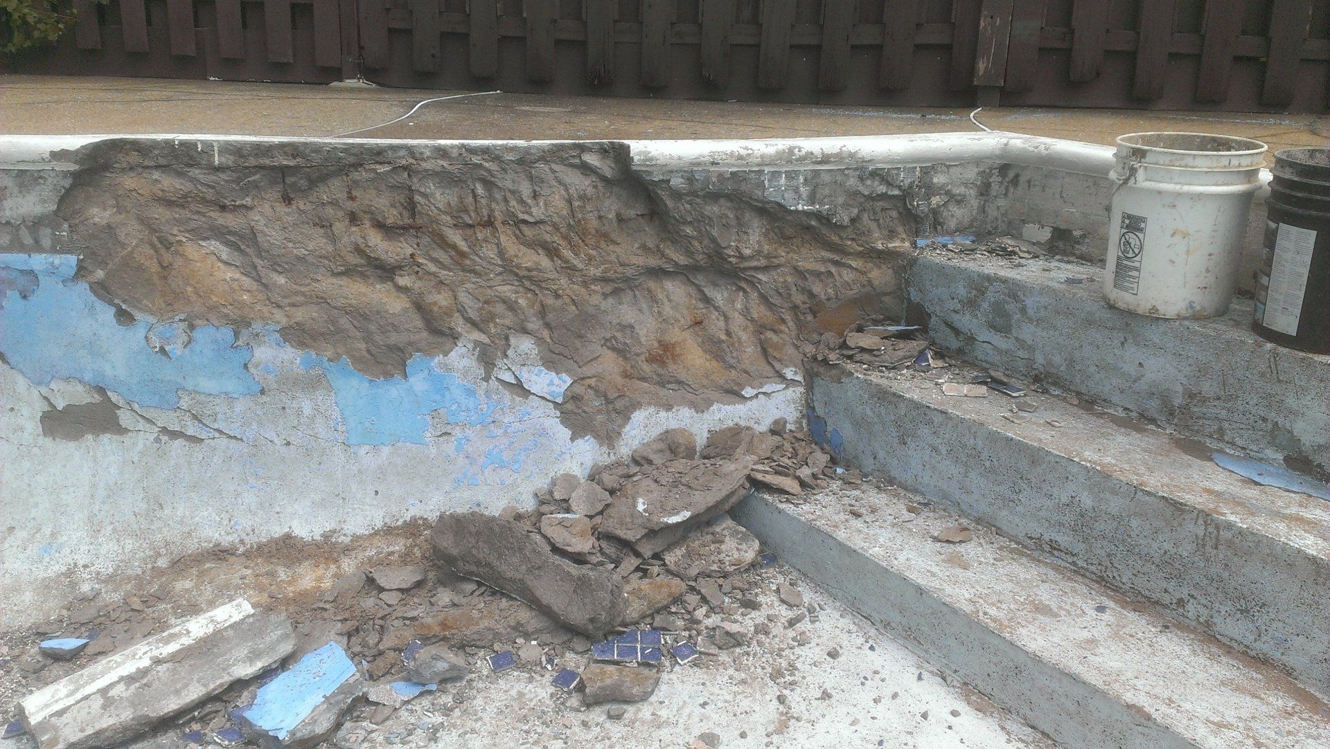 Une piscine est en cours de rénovation avec des marches en béton et un seau de terre.