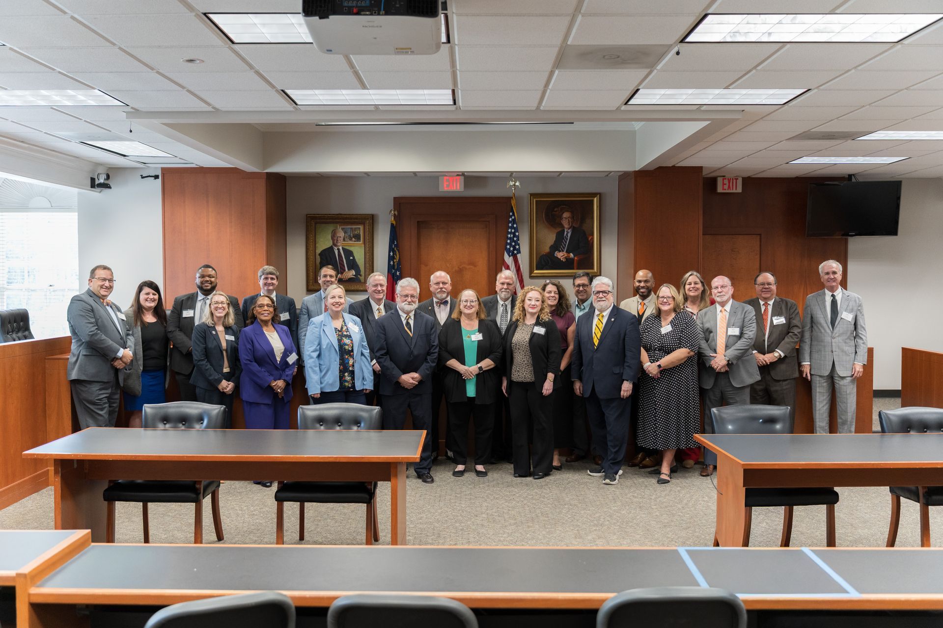 Group of people posing in a conference room, standing behind long tables under a portrait.