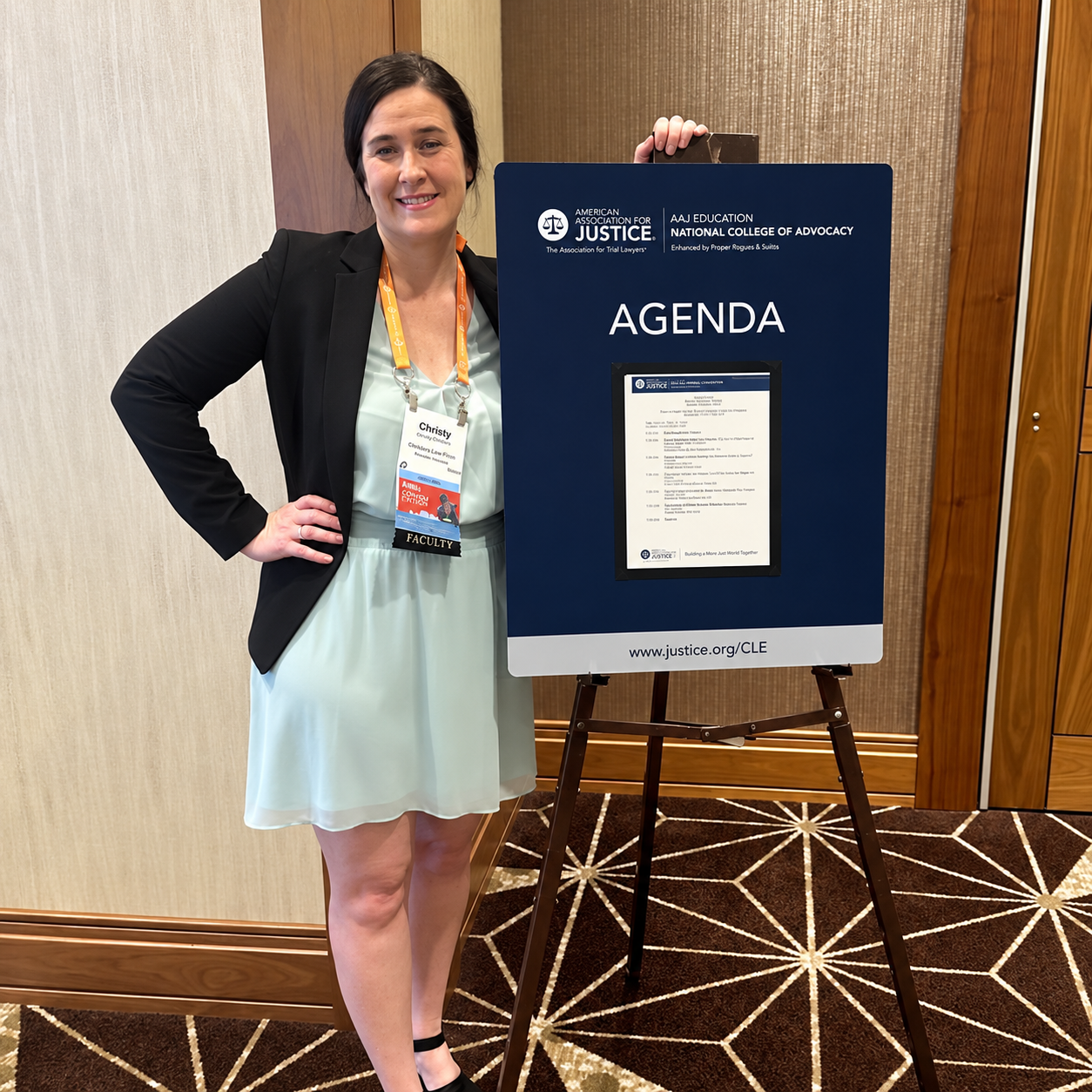 Woman standing beside an agenda sign at a conference in a hotel hallway.