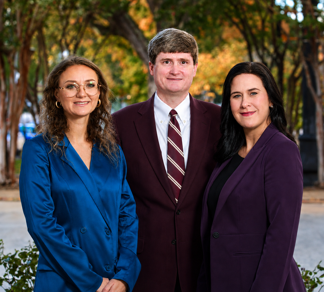 Three people in business attire standing outdoors, posing in front of a blurred green background.