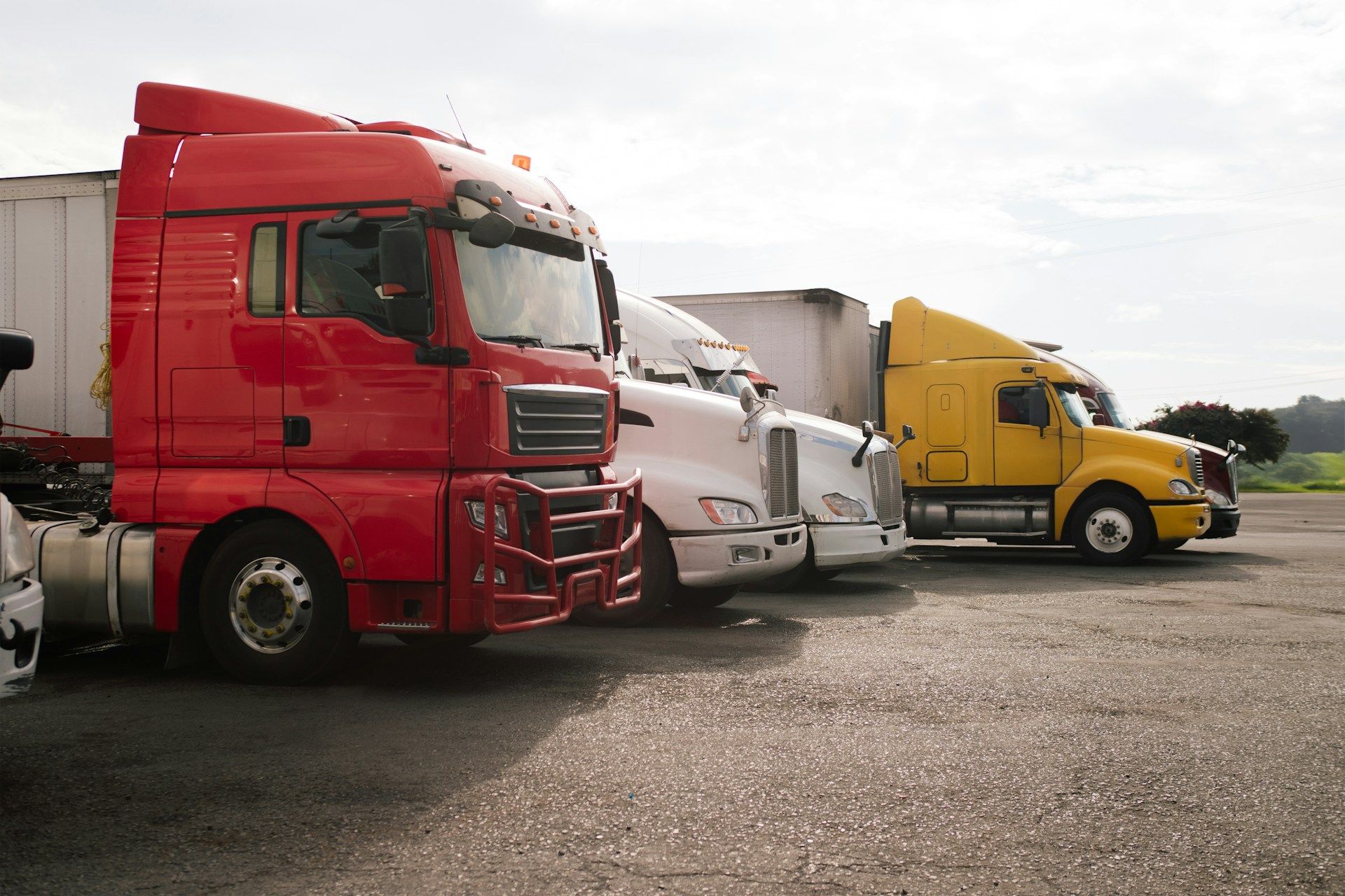 Three parked semi trucks in red, white, and yellow lined up on a gravel lot