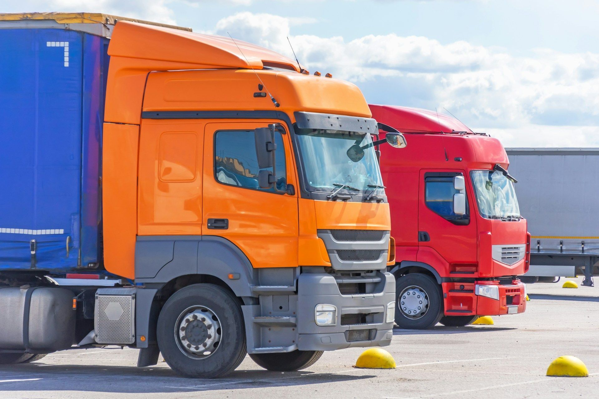 Orange and red semi-trucks parked in a lot with blue sky and clouds