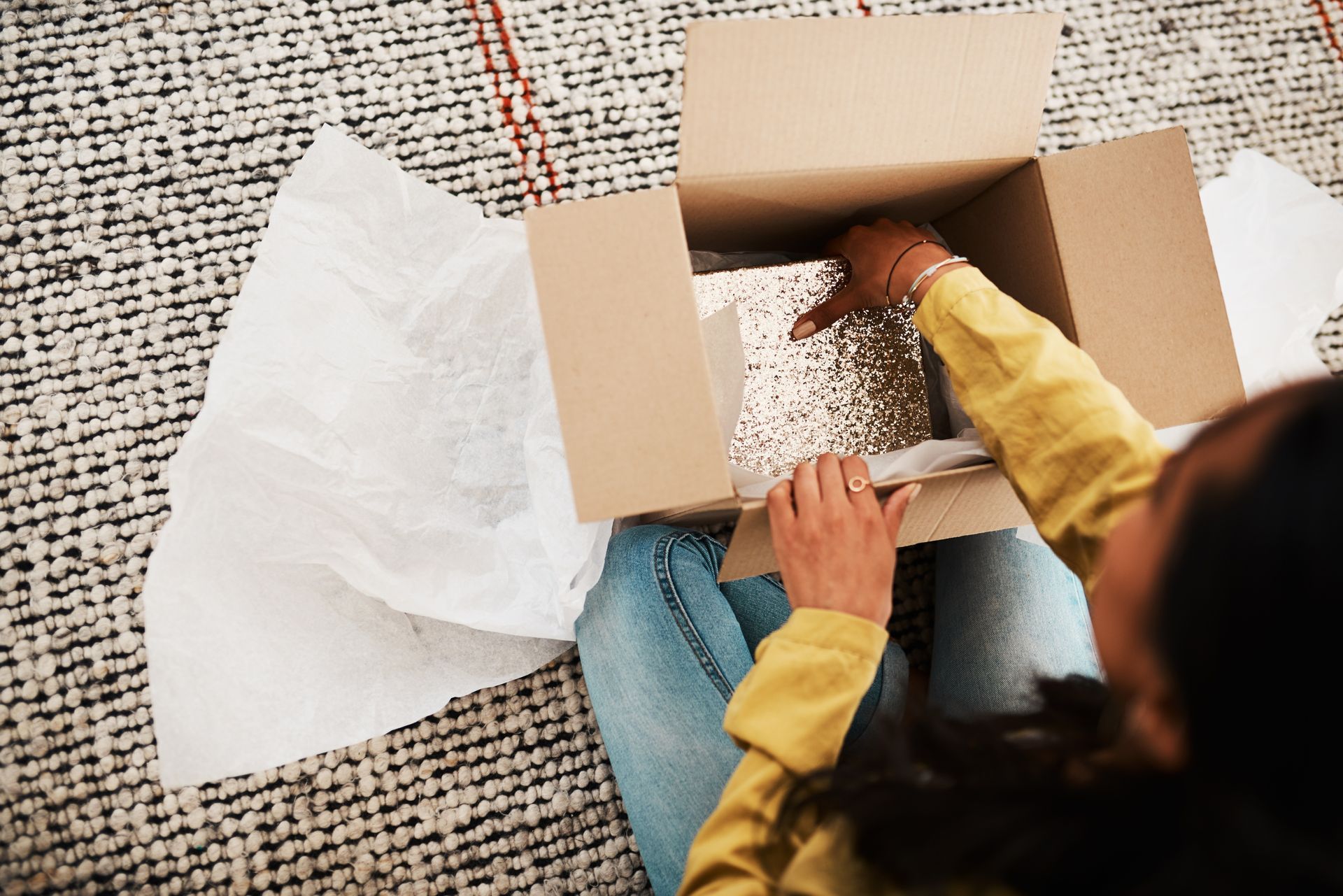 Person unpacking tissue paper from a cardboard box on a carpeted floor