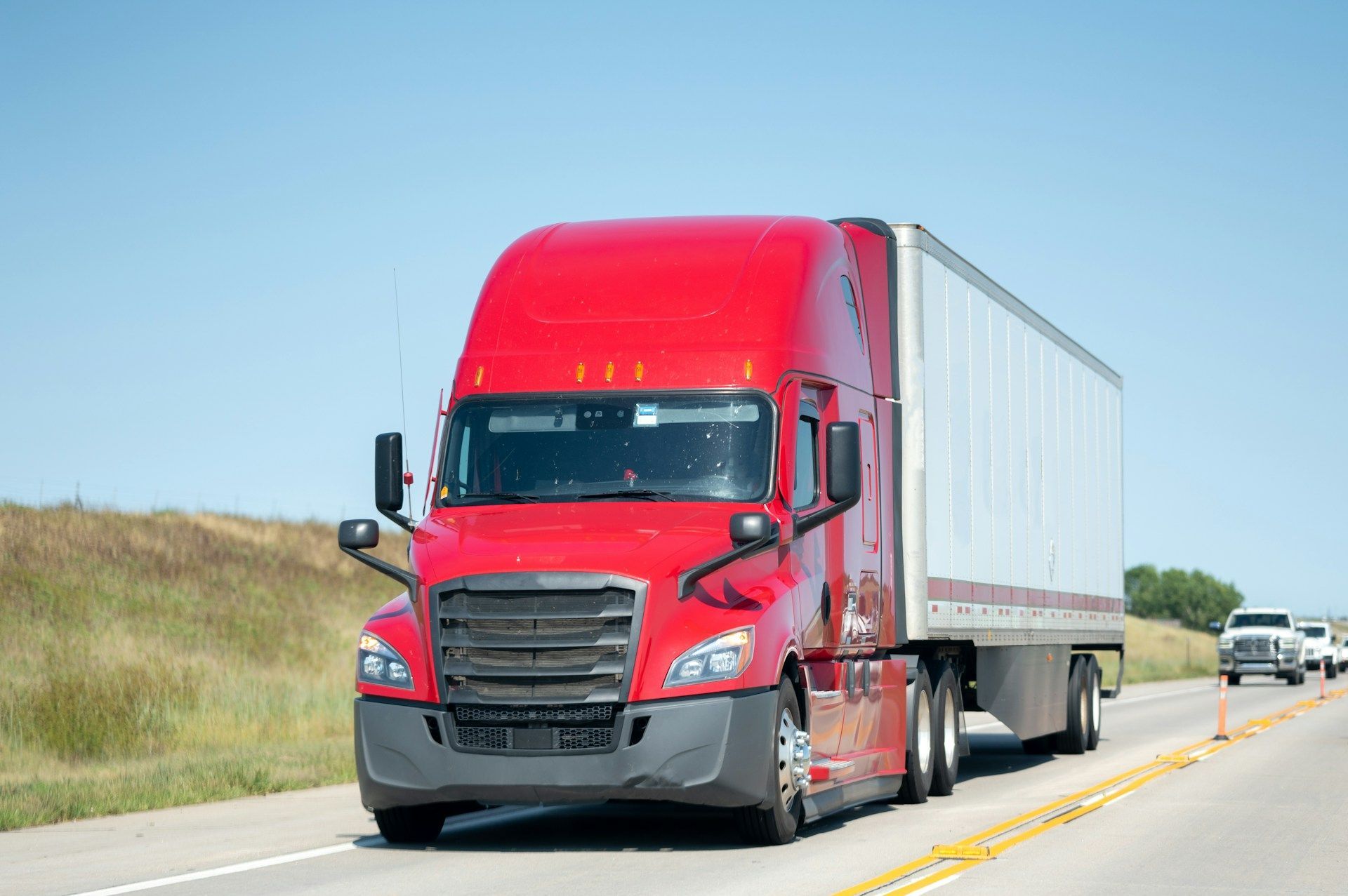Red semi-truck hauling a white trailer on a highway under a clear blue sky