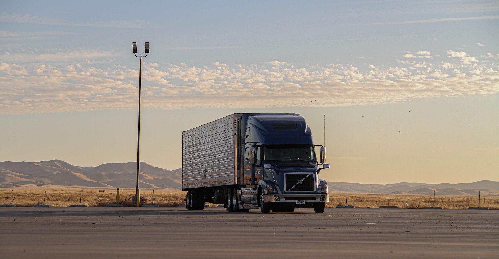 Blue semi-truck parked on a desert road at sunset with mountains in the background