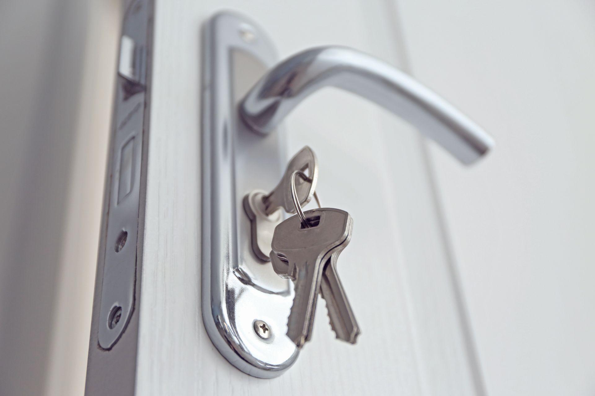 Silver door handle with keys inserted in the lock on a white door Silver door handle with keys inserted in the lock on a white door