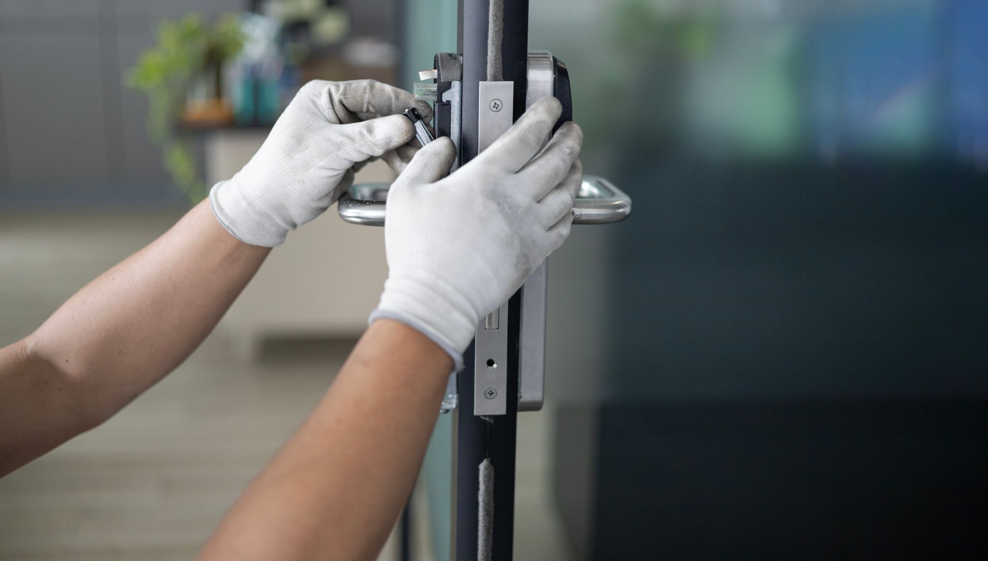 Gloved hands adjusting a door lock on a glass door panel
