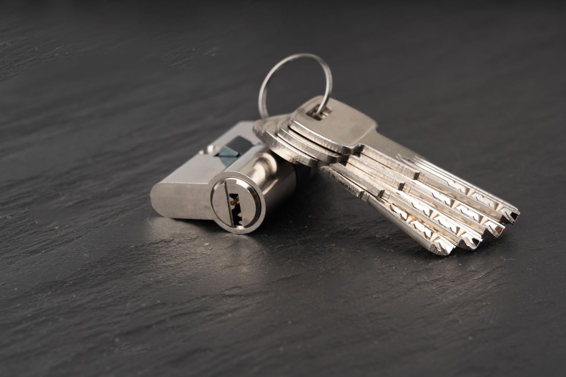 Silver keys on a keyring with a small lock resting on a dark surface