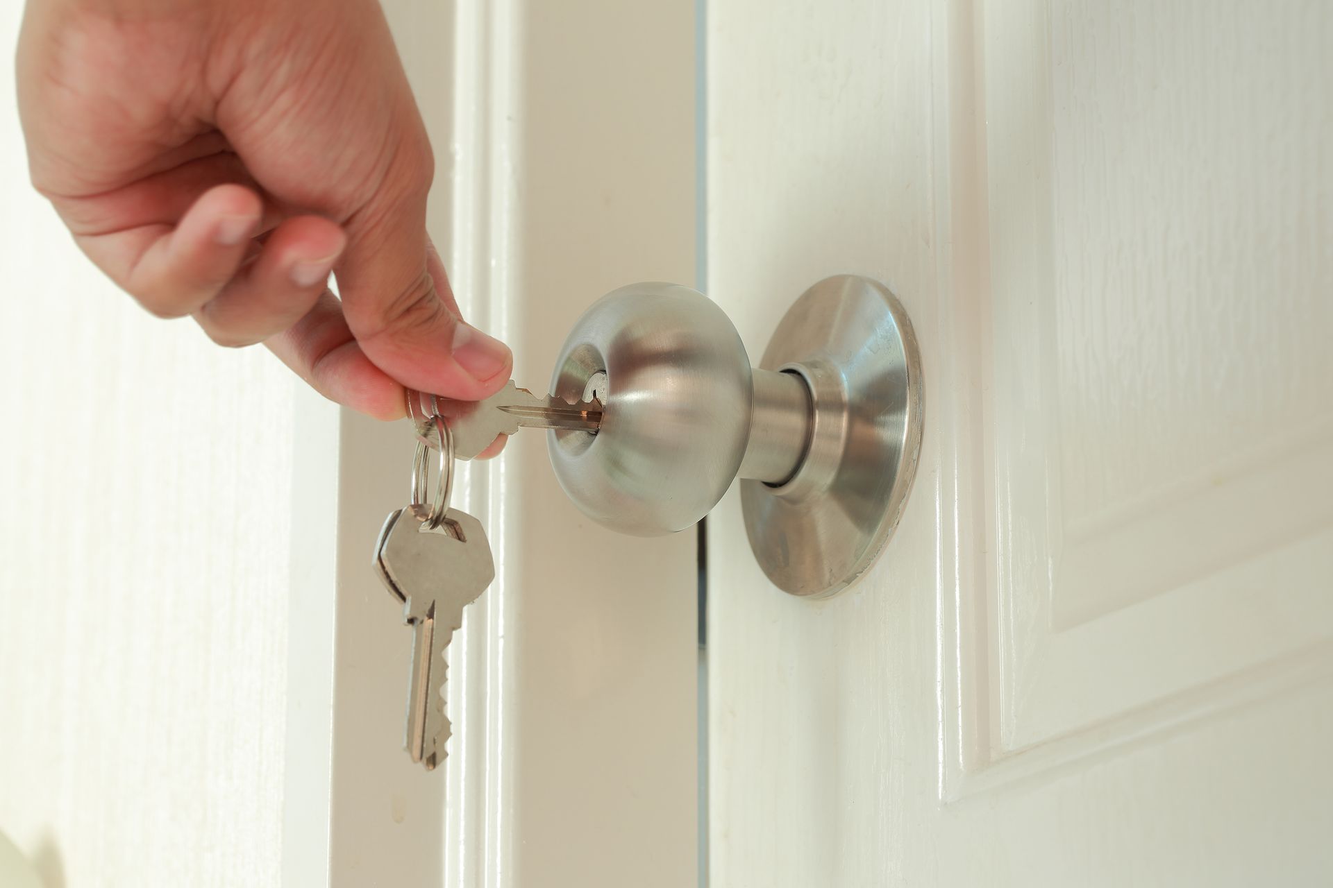 Hand turning a key in a silver door lock on a white door Hand turning a key in a silver door lock on a white door
