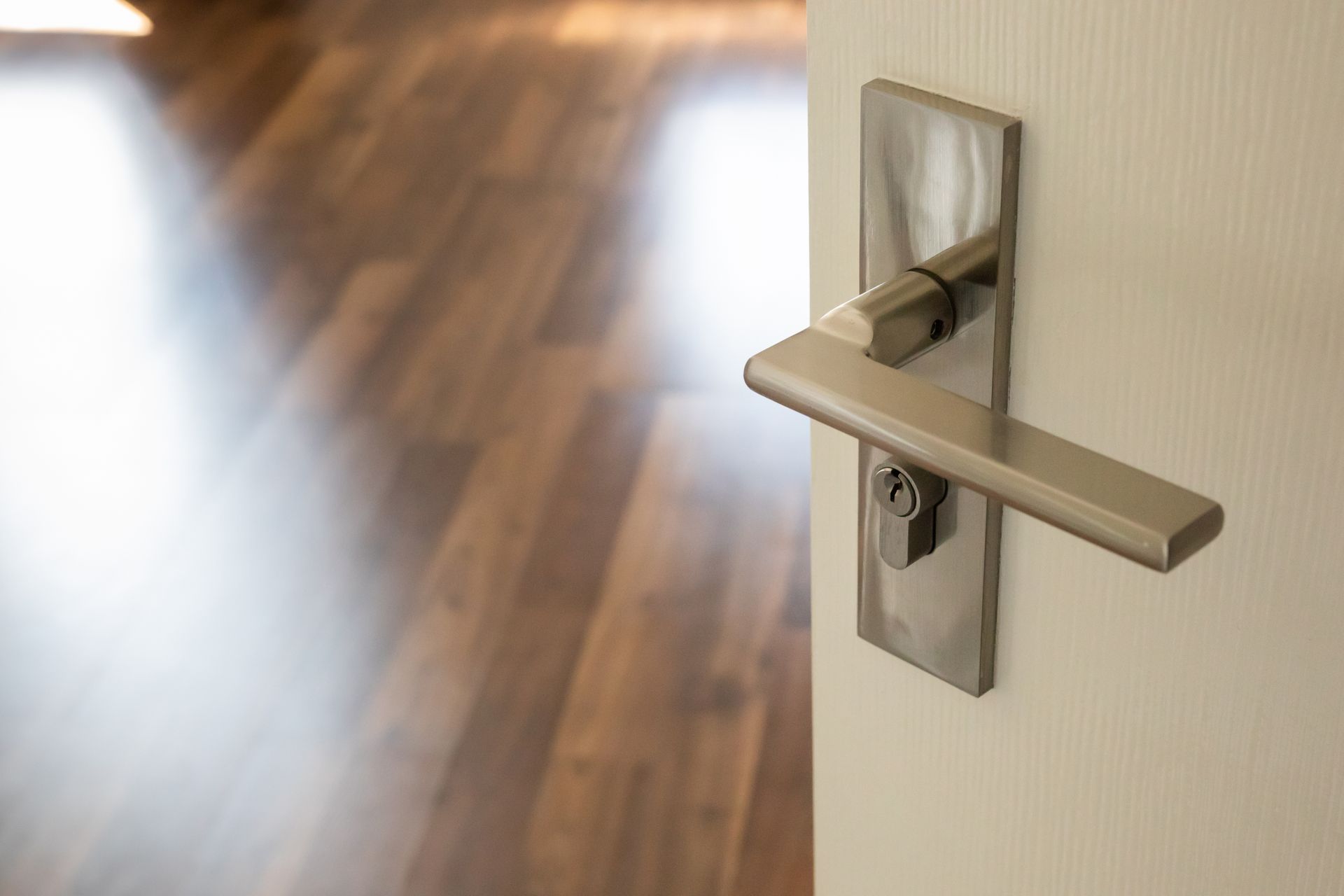 Close-up of a modern silver door handle on a white door with a wooden floor in the background