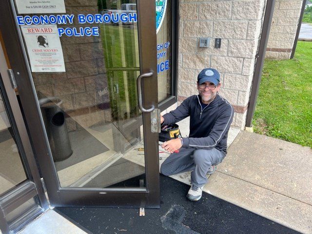 Man crouching by a police station entrance, holding the door open on a rainy day.