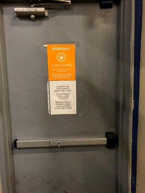 Gray emergency exit door with orange and white warning notice and push bar.