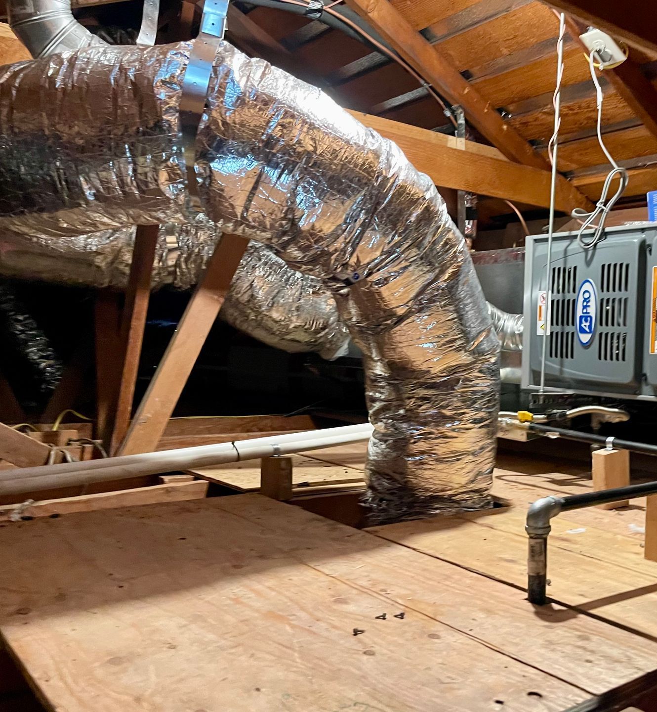 a large aluminum pipe is hanging from the ceiling of an attic .