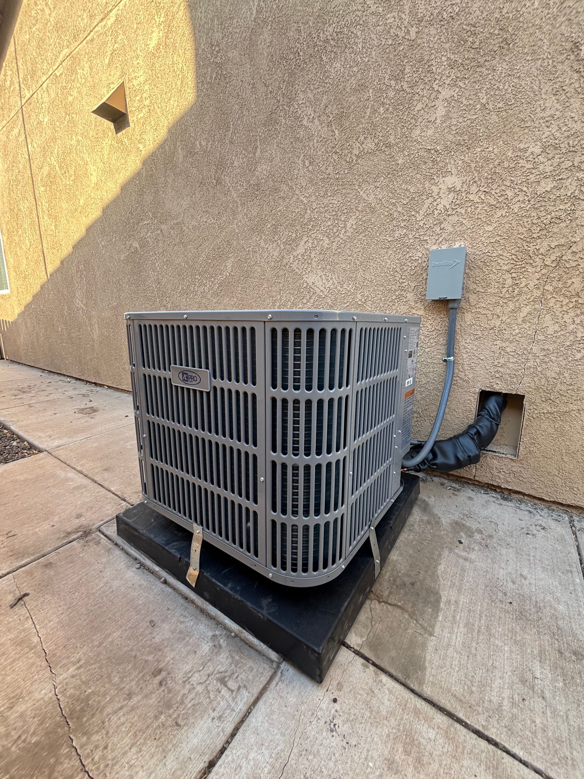 An outdoor air conditioning unit on a black platform near a stucco wall.