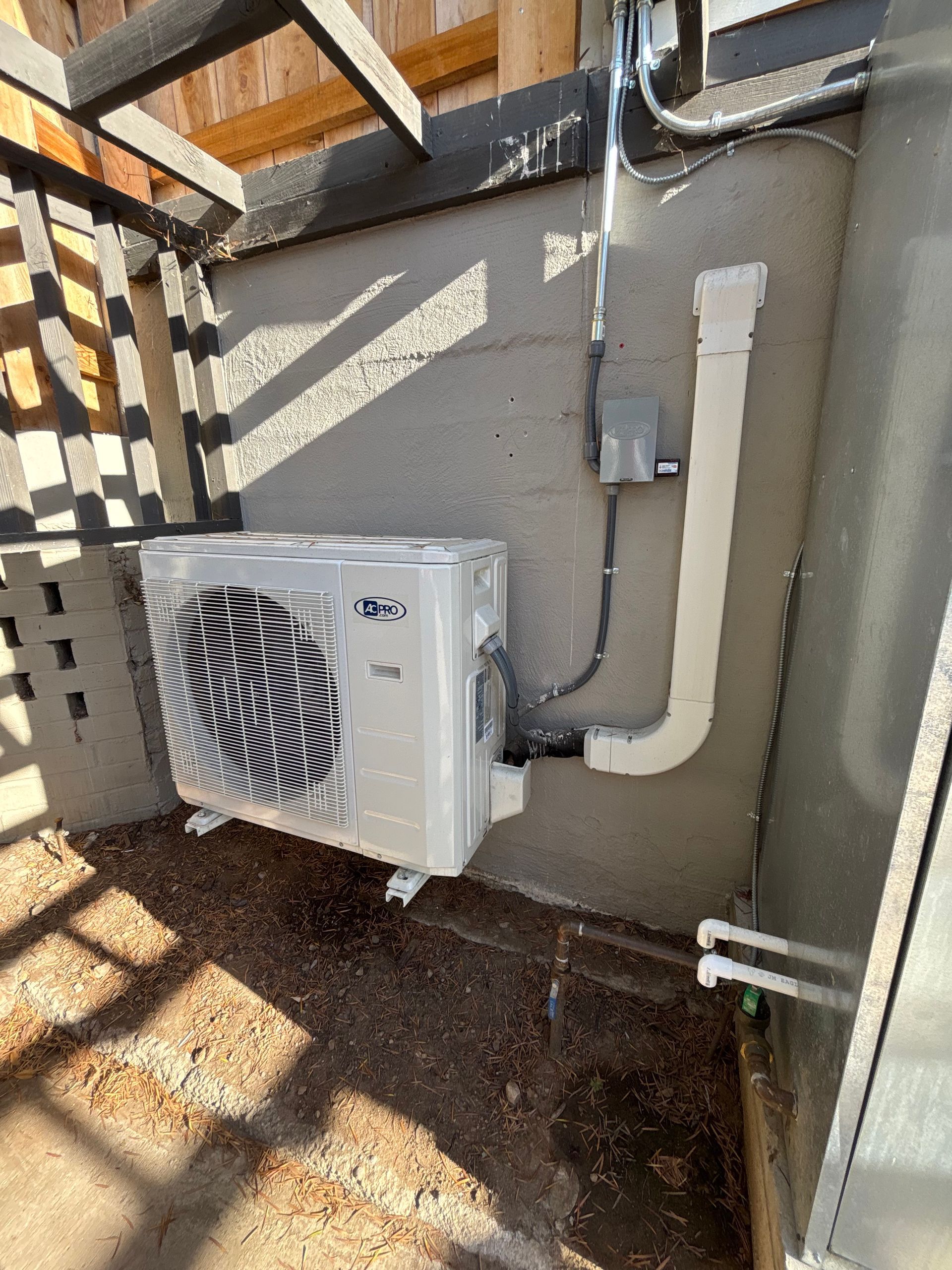 An air conditioning unit mounted on a concrete wall, with white vent pipes and wiring.