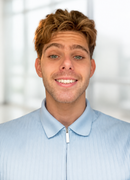 Smiling young man in a light blue collared shirt against a bright blurred background