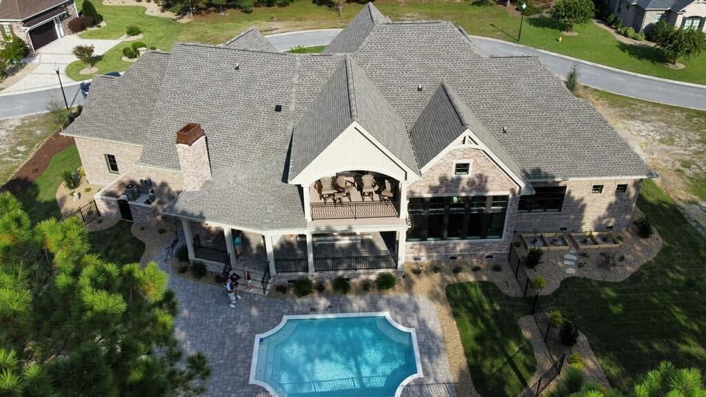Aerial view of a large stone house with a backyard pool and landscaped lawn.