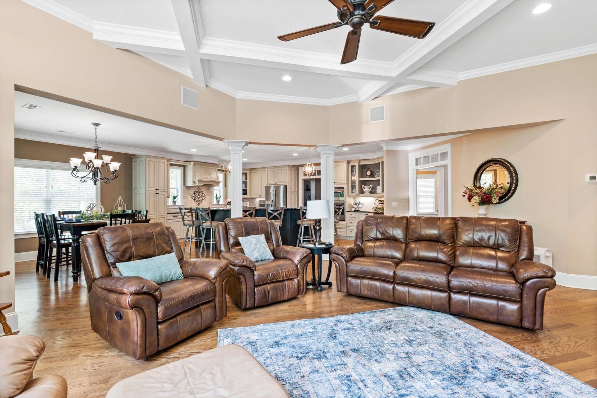 Spacious living room with brown leather sofas, blue rug, and ceiling fan beneath tray ceiling