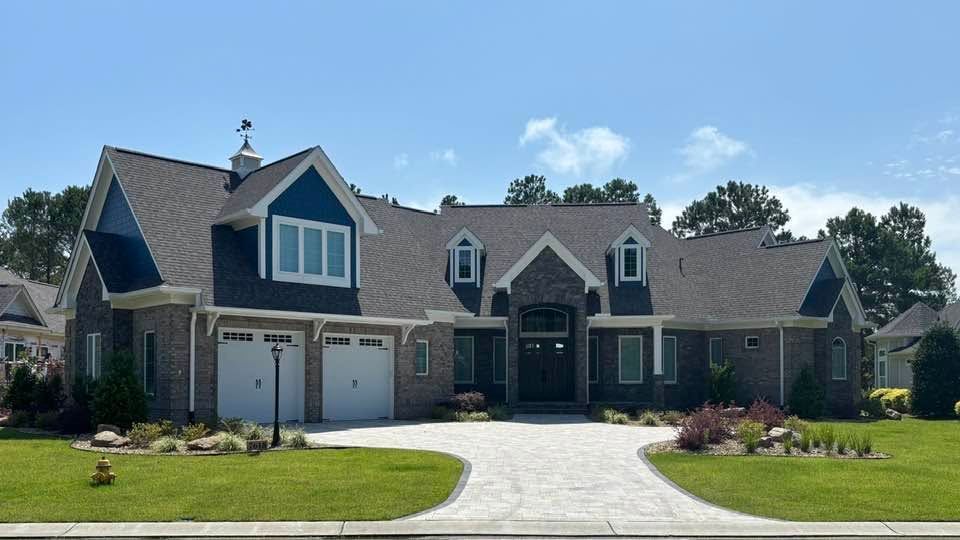 Large suburban house with stone facade, twin garages, and a wide curved driveway under a blue sky