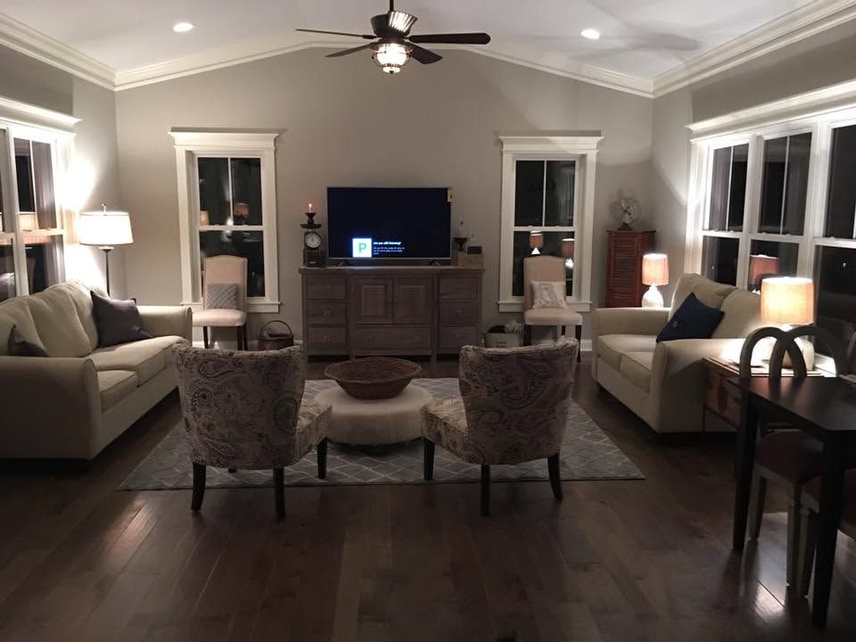 Living room with beige sofas, two chairs, TV console, lamps, and ceiling fan in a symmetrical layout.
