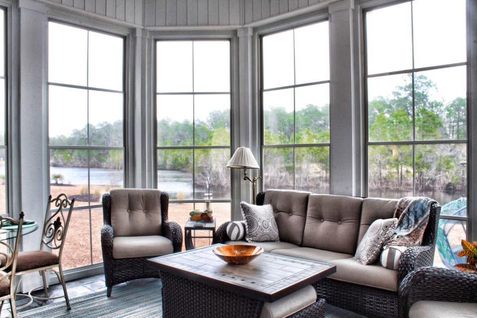 Bright living room with gray seating, a coffee table, and large bay windows overlooking water and trees