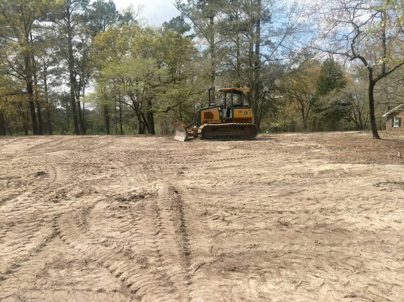 Bulldozer grading a cleared dirt lot with trees in the background