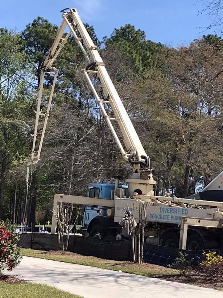 Concrete pump truck raising boom over a driveway surrounded by trees and bushes