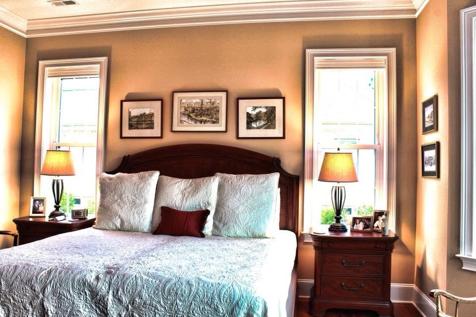 Sunlit bedroom with a large bed, bedside lamps, and framed wall art on beige walls