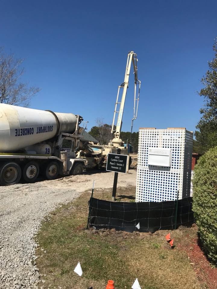Concrete truck pumping at a construction site beside a white utility box and black fencing under a blue sky