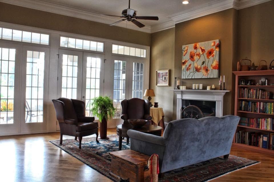 Living room with large windows, gray sofa, two armchairs, fireplace, bookshelf, and colorful wall art