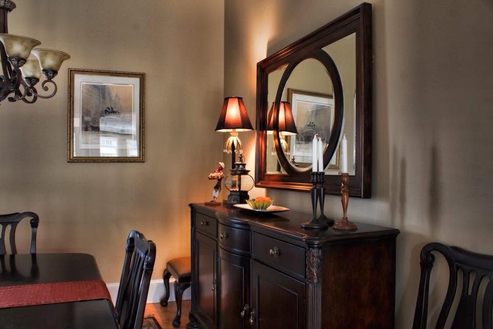 Dining room with dark wood sideboard, mirror, lamps, and framed wall art in warm lighting