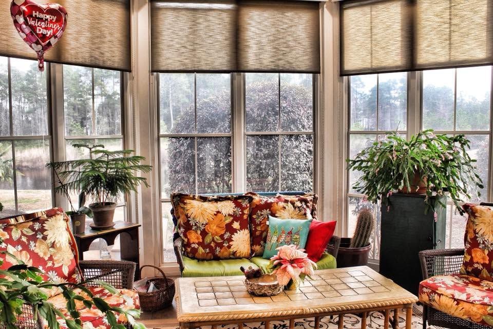 Sunlit sunroom with bay windows, wicker seating, and colorful floral cushions around a coffee table
