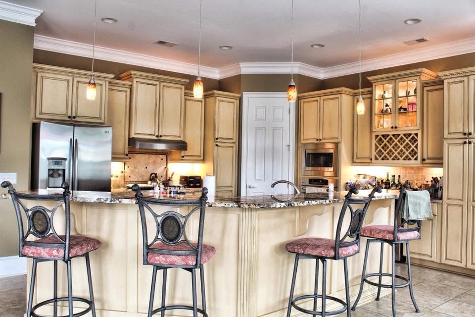 Bright kitchen with granite island, bar stools, stainless appliances, and cream cabinets