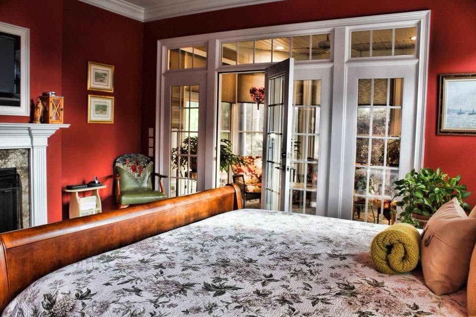 Bedroom with red walls, French doors, a wooden bed, floral bedding, and a fireplace.
