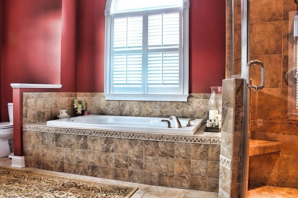 Luxurious marble bathroom with a white soaking tub, red walls, and a window above the bath