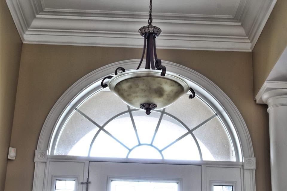Hanging lantern chandelier above an arched window in a beige entryway
