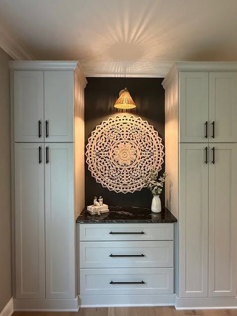 Built-in white cabinets framing a black alcove with a decorative mandala wall hanging and dresser.