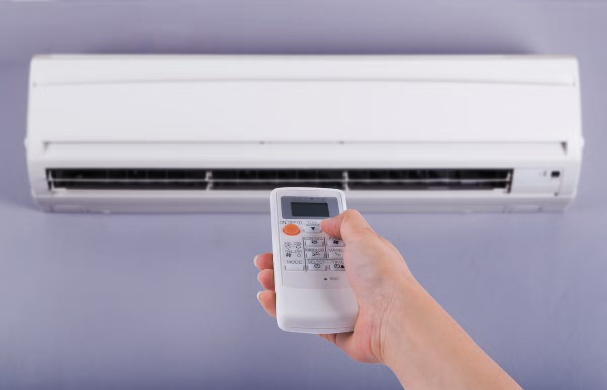 A person is holding a remote control in front of an air conditioner.