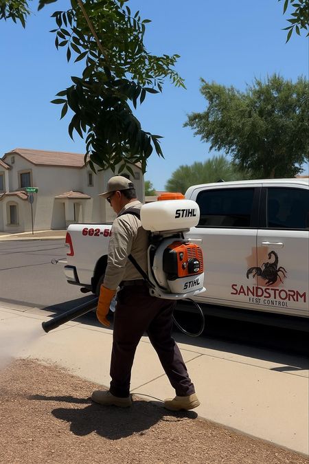 Worker using a STT backpack sprayer beside a white truck on a sunny suburban street