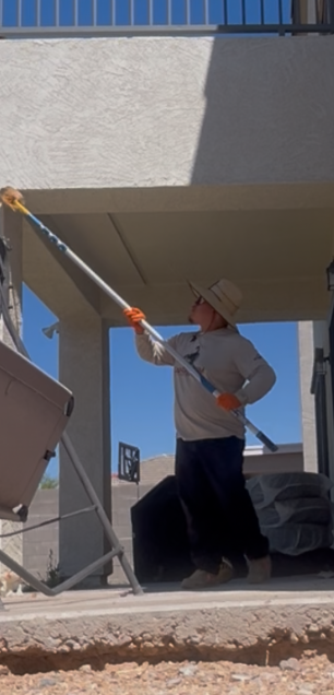 Person using a long-handled paint roller to paint a building exterior under a balcony.