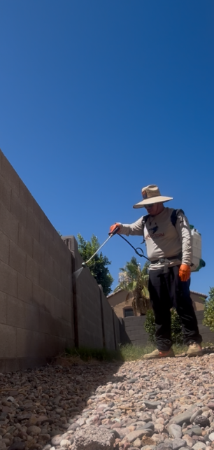 Person in a straw hat raking gravel beside a wall under a clear blue sky.