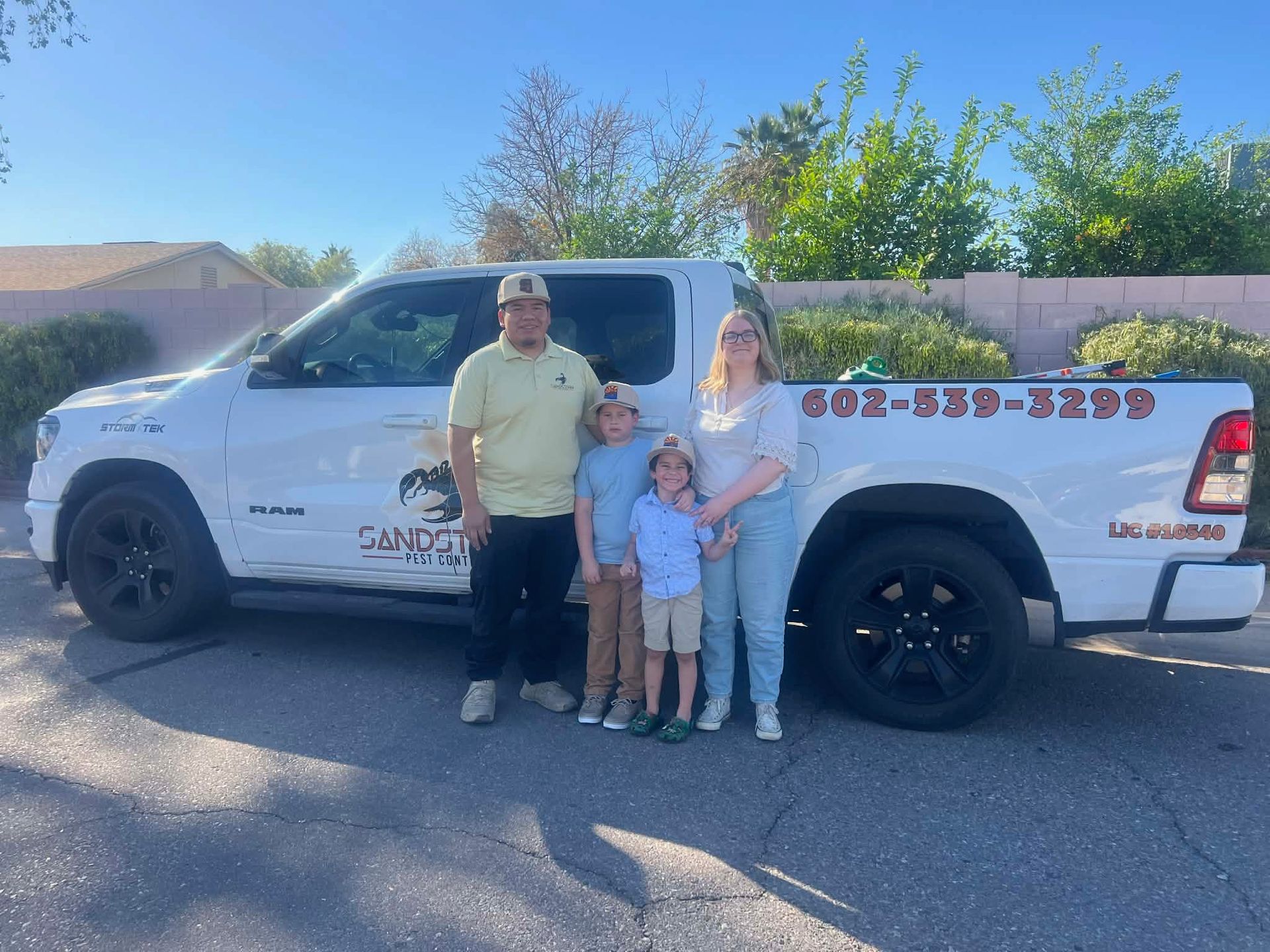 Three people posing beside a white pickup truck in a sunny parking lot.