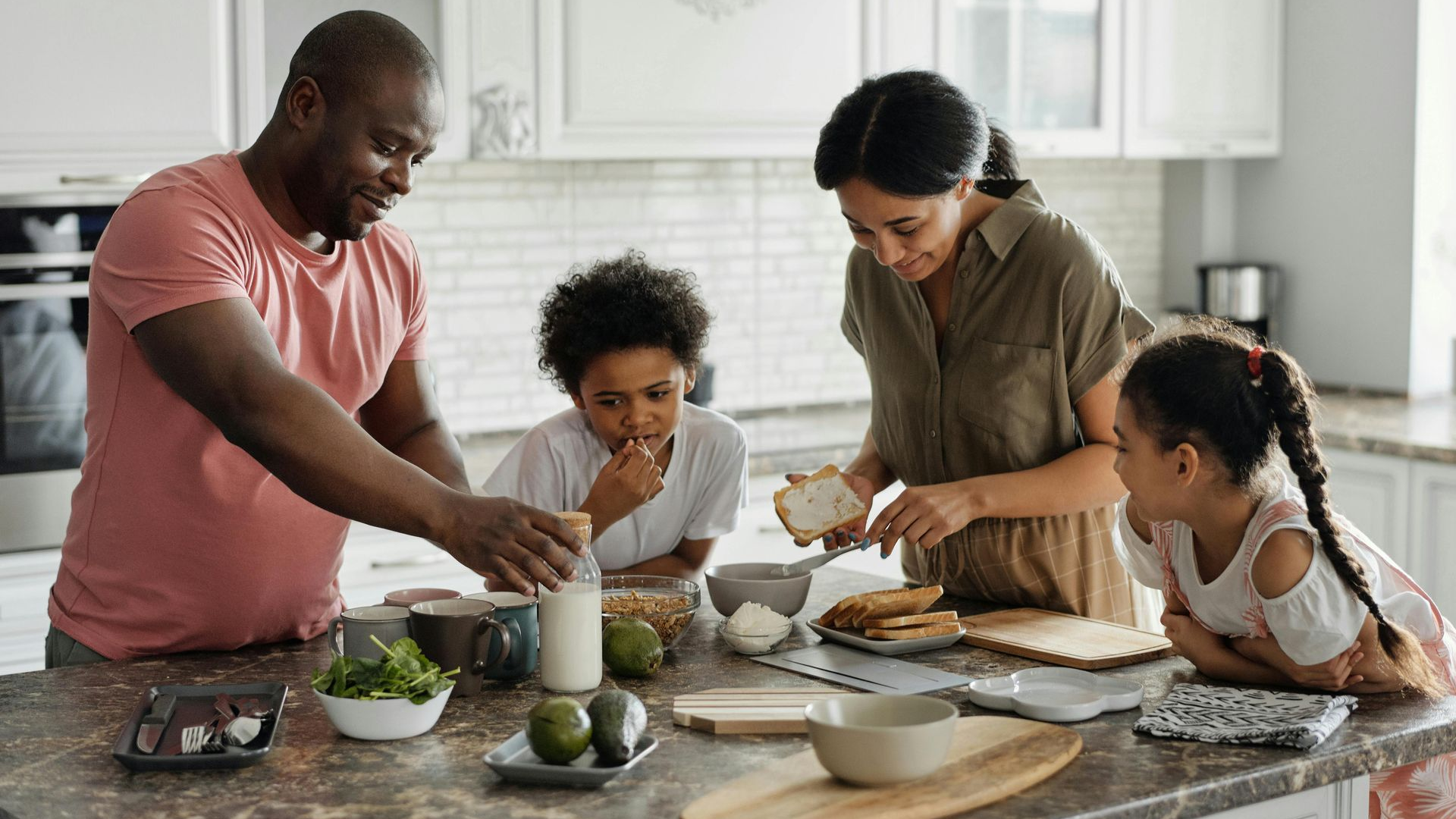 Family preparing food in a kitchen. Adults and children interact, focused on the counter with ingredients and utensils.
