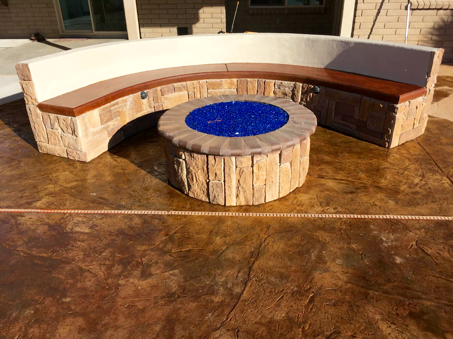 A fire pit is surrounded by a curved bench on a patio.