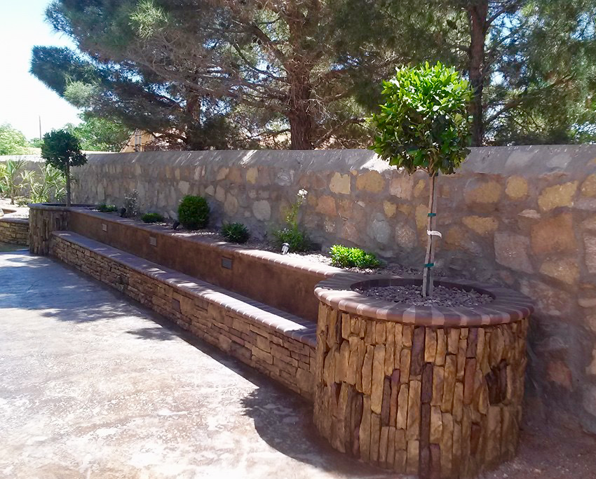 A stone wall with planters and trees in front of it