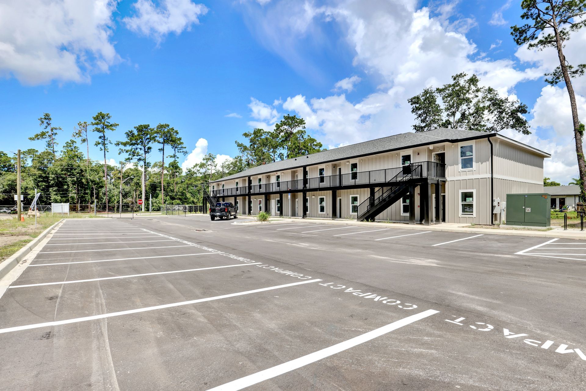 Two-story building with exterior stairwells and parking lot under a blue sky with clouds.