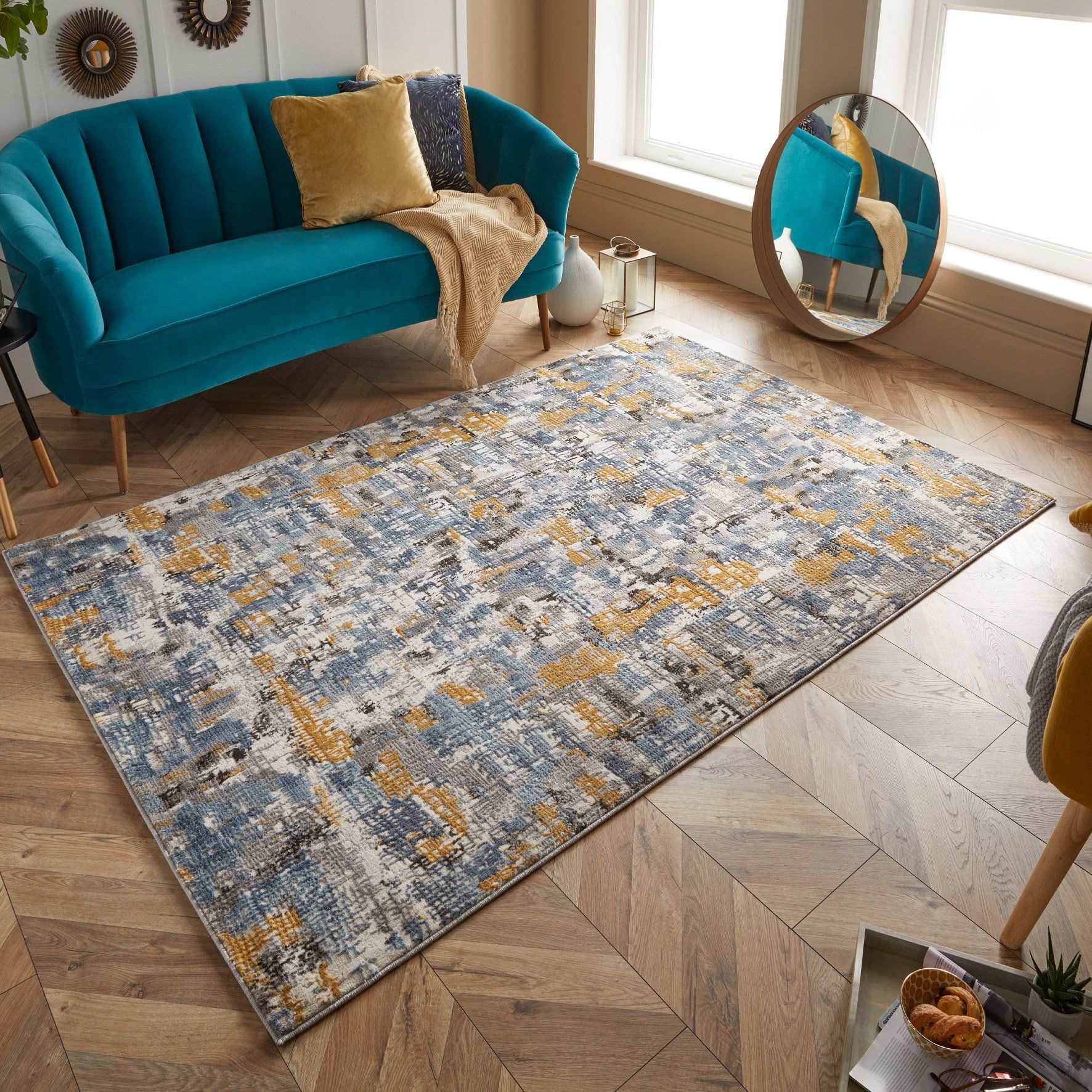Teal sofa and abstract patterned rug in a light-filled living room with wooden floors.
