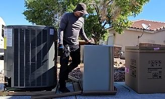 Technician standing beside outdoor HVAC units and a box in a residential yard