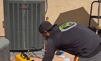 Worker kneels beside an outdoor HVAC unit, using tools on a patio during maintenance.